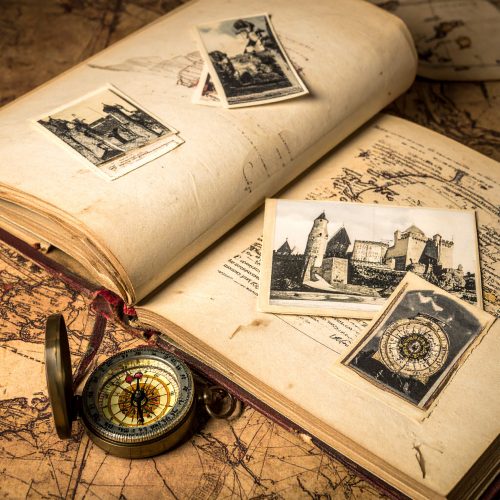 Un mapa antiguo extendido sobre el que reposa un libro de viajes abierto, fotografías de castillos antiguos y una brújula de latón.